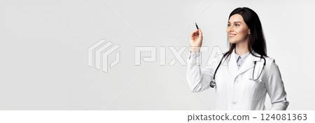 A smiling woman doctor in a white lab coat writes with a pen on a white background. A smiling woman doctor in a white lab coat writes with a pen on a white background. 124081363