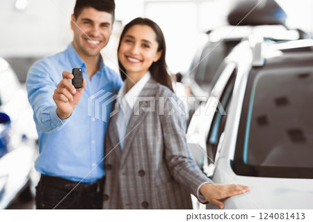 Buying Automobile Concept. Young Couple Hugging In Dealership Store, Man Showing New Car Key, Free Space Buying Automobile Concept. Young Couple Hugging In Dealership Store, Man Showing New Car Key, Free Space 124081413