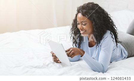 African pretty girl reading blog on digital tablet lying in bed, free space African pretty girl reading blog on digital tablet lying in bed, free space 124081433