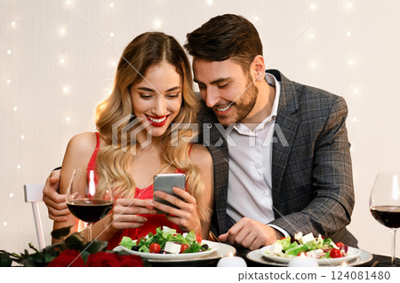 Young Couple Using Smartphone Together During Romantic Dinner In Restaurant, Browsing Internet, Social Networks Or Watching Photos. Free Space 124081480