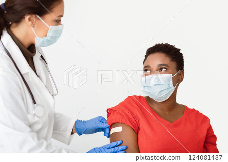 Covid-19 Vaccination. Black Woman Getting Vaccinated Against Coronavirus, Doctor Sticking Adhesive Plaster Strip After Corona Virus Vaccine Injection Shot On White Studio Background, Wearing Face Mask 124081487