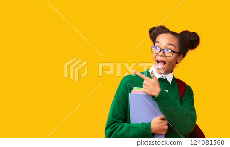 Great Offer. Excited afro teenage girl in glasses pointing at copyspace, holding folders, wearing backpack, panorama 124081560