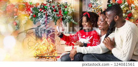 Little black girl taking selfie with parents near Christmas tree, enjoying winter holidays together 124081561