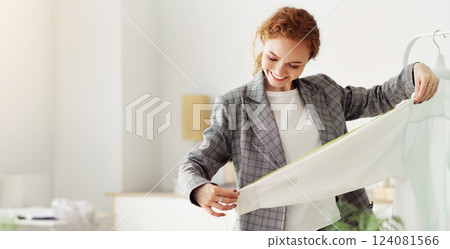 Dressmaking Concept. Smiling red-haired seamstress working at home, measuring sleeve length on rack, copy space Dressmaking Concept. Smiling red-haired seamstress working at home, measuring sleeve length on rack, copy space 124081566