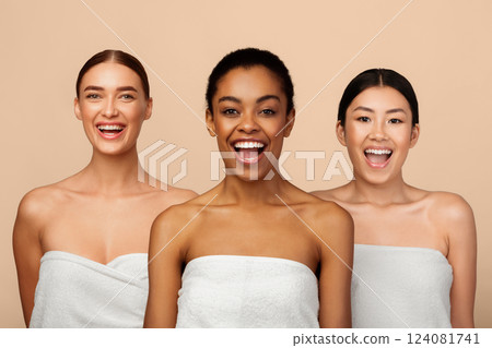 Playful Multiethnic Model Girls Posing Wrapped In White Bath Towels Standing Over Gray Background, Smiling To Camera. 124081741