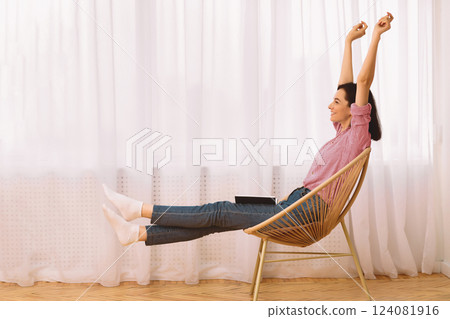 Weekends Finally. Young woman raising hands sitting in modern chair with a book on her lap, stretching body, copyspace 124081916