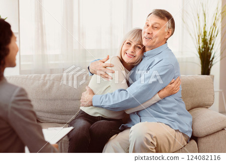 Psychotherapy. Happy senior couple sitting on couch and hugging, smiling female doctor listening, copyspace 124082116