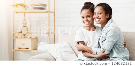 Two beautiful black sisters hugging each other at home, copy space 124082181