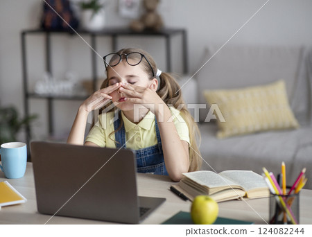 Tired schoolgirl rubbing her dry irritated eyes while studying online on laptop at home, copy space. Teen female student exhausted from looking at screen, doing assignments or communicating on web 124082244