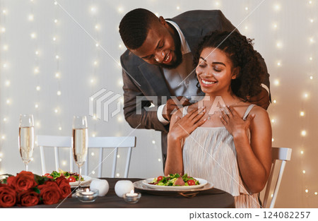 Gallant african american man putting golden necklace on his woman, having valentine dinner at restaurant, empty space Gallant african american man putting golden necklace on his woman, having valentine dinner at restaurant, empty space 124082257