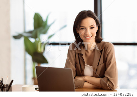Young Entrepreneur. Portrait of beautiful girl sitting at desk with folded arms, looking at camera, free space 124082292