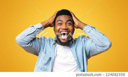 Wow. Excited african american guy holding hands on head, looking at camera with amazement, yellow studio background 124082350