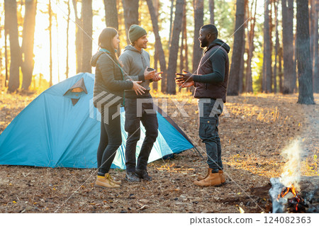 Back view of three friends camping in autumn forest, planning next trip, free space Back view of three friends camping in autumn forest, planning next trip, free space 124082363