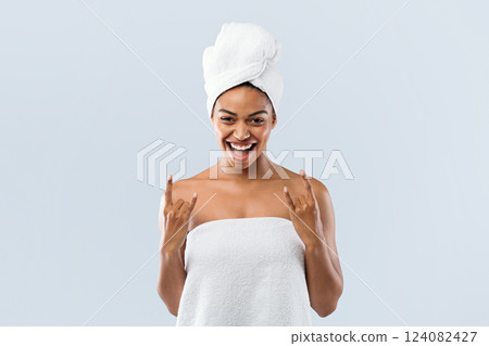 Portrait of happy young black woman wrapped in bath towels showing cool gesture over grey studio background 124082427