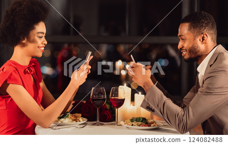 Modern Relationship. Happy Afro Couple Using Smartphones During Romantic Date In Restaurant. Panorama Modern Relationship. Happy Afro Couple Using Smartphones During Romantic Date In Restaurant. Panorama 124082488