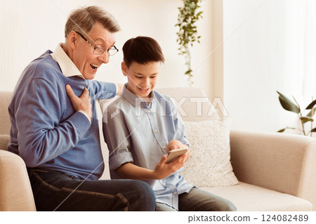 Happy Grandson Teaching Grandpa To Use Mobile Phone Sitting On Sofa At Home. Empty Space Happy Grandson Teaching Grandpa To Use Mobile Phone Sitting On Sofa At Home. Empty Space 124082489