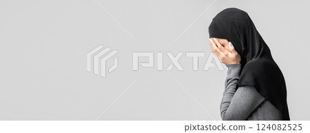 Profile portrait of crying muslim woman in hijab covering her face with hands in despair, suffering from abuse or discrimination, gray background 124082525