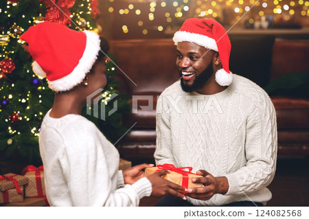 Romantic black couple in Santa hats presenting gifts to each other while celebrating christmas at home Romantic black couple in Santa hats presenting gifts to each other while celebrating christmas at home 124082568