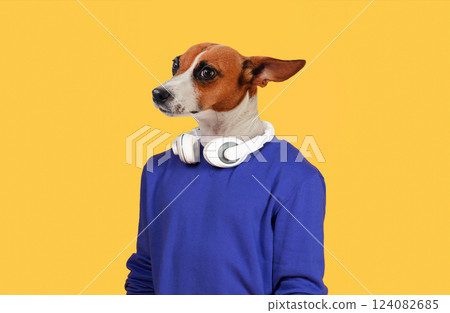 A dog with a brown and white coat wears white headphones over a blue sweatshirt against a yellow background. The dog's head is tilted slightly, and its ears are perked up A dog with a brown and white coat wears white headphones over a blue sweatshirt against a yellow background. The dog's head is tilted slightly, and its ears are perked up 124082685
