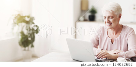 Smiling senior business woman looking at laptop, working from home, panorama with empty space Smiling senior business woman looking at laptop, working from home, panorama with empty space 124082692