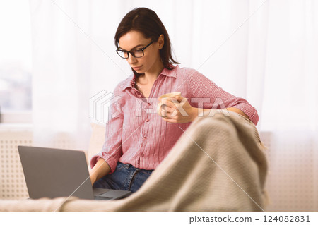 Freelance. Casual beautiful young woman in eyeglasses working on a laptop sitting on the couch at home, copyspace Freelance. Casual beautiful young woman in eyeglasses working on a laptop sitting on the couch at home, copyspace 124082831
