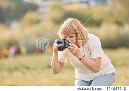 Photographer with a camera. Senior woman having nice weekend outdoors on the field at sunny day 124082848