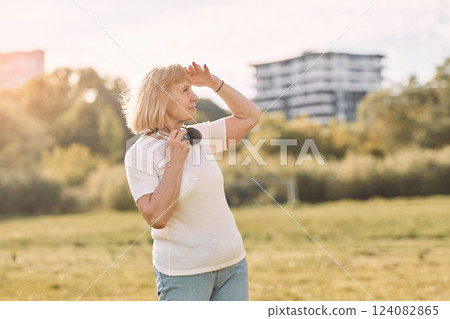 With headphones. Senior woman having nice weekend outdoors on the field at sunny day 124082865