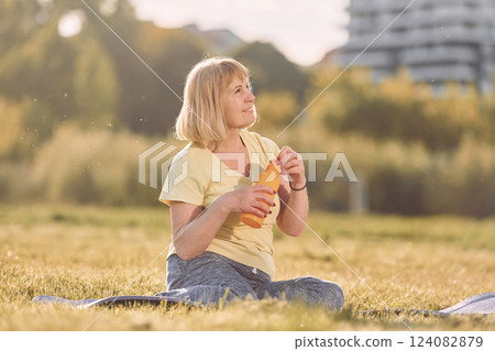 On yoga mat. Senior woman having nice weekend outdoors on the field at sunny day 124082879