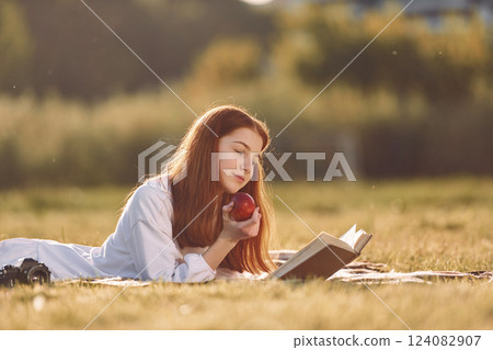 Laying down and reading the book. Young girl is on the field at sunny daytime having nice weekend Laying down and reading the book. Young girl is on the field at sunny daytime having nice weekend 124082907