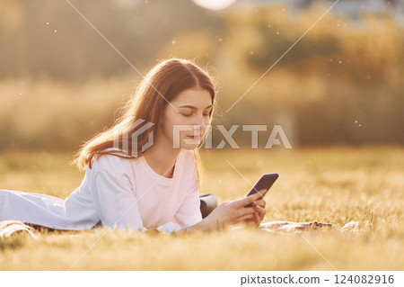 With smartphone in hands. Young girl is on the field at sunny daytime having nice weekend 124082916