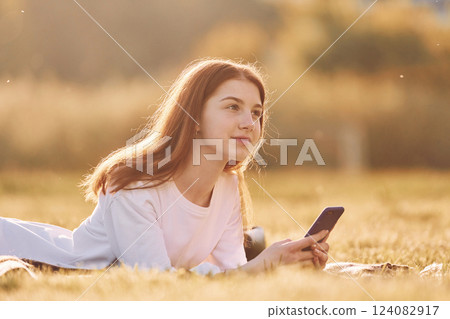 With smartphone in hands. Young girl is on the field at sunny daytime having nice weekend 124082917
