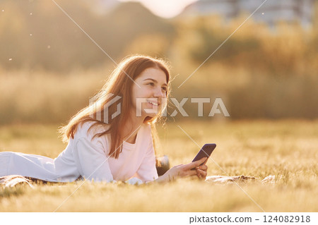 Using smartphone. Young girl is on the field at sunny daytime having nice weekend 124082918