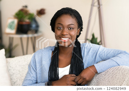 Portrait of pretty african american woman holding cup of coffee while sitting on a sofa at home and smiling to camera. Portrait of pretty african american woman holding cup of coffee while sitting on a sofa at home and smiling to camera. 124082949