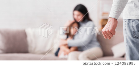 Domestic abuse. Scared woman with little daughter suffering from husband's violence, male fist in foreground, selective focus 124082993