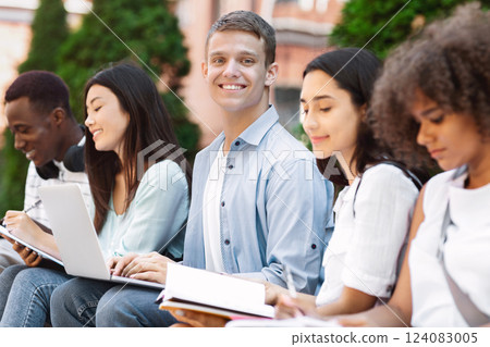 College students studying ioutdoors, preparing for exams together, selective focus on smiling teen guy 124083005