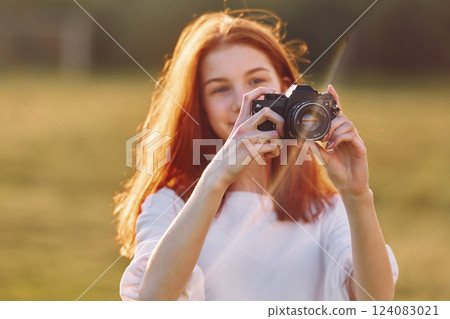 Holding camera. Young girl is on the field at sunny daytime having nice weekend 124083021