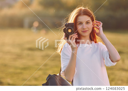 Professional camera in hands. Young girl is on the field at sunny daytime having nice weekend 124083025