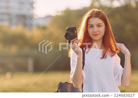 Professional camera in hands. Young girl is on the field at sunny daytime having nice weekend 124083027