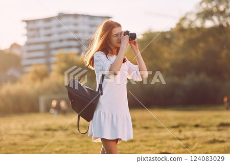 Professional camera in hands. Young girl is on the field at sunny daytime having nice weekend Professional camera in hands. Young girl is on the field at sunny daytime having nice weekend 124083029