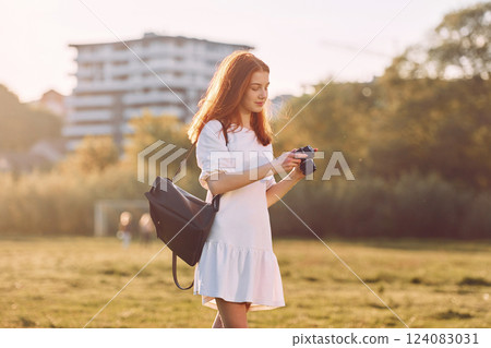 Professional camera in hands. Young girl is on the field at sunny daytime having nice weekend Professional camera in hands. Young girl is on the field at sunny daytime having nice weekend 124083031