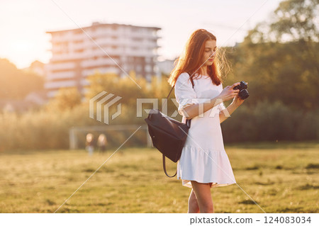 Professional camera in hands. Young girl is on the field at sunny daytime having nice weekend Professional camera in hands. Young girl is on the field at sunny daytime having nice weekend 124083034