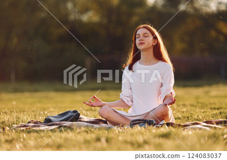 Doing yoga on the mat. Young girl is on the field at sunny daytime having nice weekend Doing yoga on the mat. Young girl is on the field at sunny daytime having nice weekend 124083037