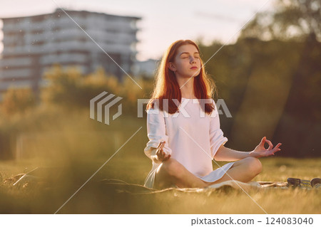 Doing yoga on the mat. Young girl is on the field at sunny daytime having nice weekend Doing yoga on the mat. Young girl is on the field at sunny daytime having nice weekend 124083040