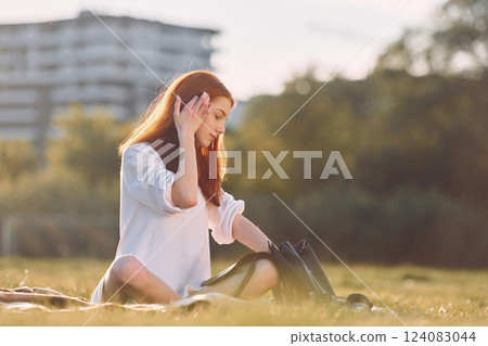 Sitting on the plaid with bag. Young girl is on the field at sunny daytime having nice weekend 124083044