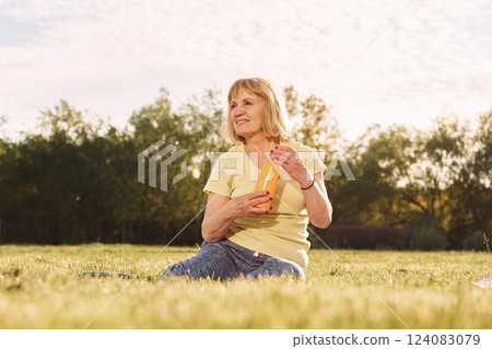 Orange bottle in the hands. Senior woman having nice weekend outdoors on the field at sunny day 124083079