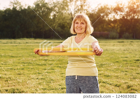 Making stretches for the hands. Senior woman having nice weekend outdoors on the field at sunny day 124083082