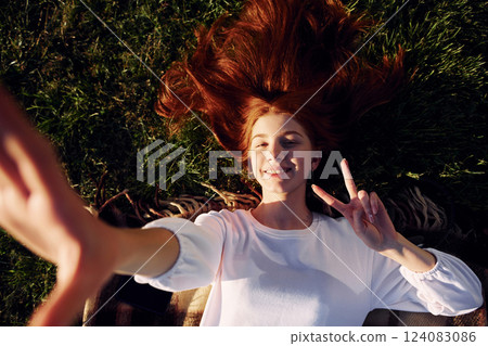 Laying down and making a selfie. Top view. Young girl is on the field at sunny daytime having nice weekend 124083086