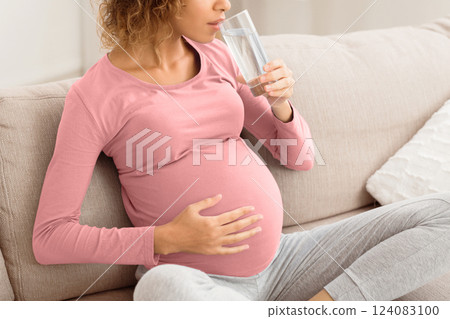 Pregnant woman drinking water sitting on sofa, resting at home. Pregnancy, healthcare, thirst concept 124083100