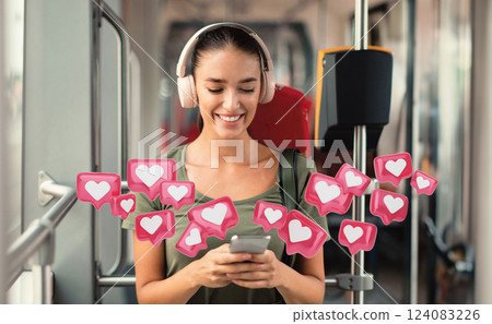 A woman sits on public transportation, using her smartphone while wearing headphones. She is smiling and appears to be enjoying her time. A number of pink heart icons are floating around her A woman sits on public transportation, using her smartphone while wearing headphones. She is smiling and appears to be enjoying her time. A number of pink heart icons are floating around her 124083226