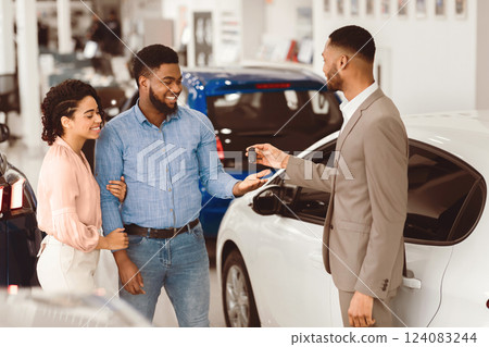Buying Auto. Salesman Giving Car Key To Buyers For Test Drive Standing In Luxury Dealership Center. Buying Auto. Salesman Giving Car Key To Buyers For Test Drive Standing In Luxury Dealership Center. 124083244